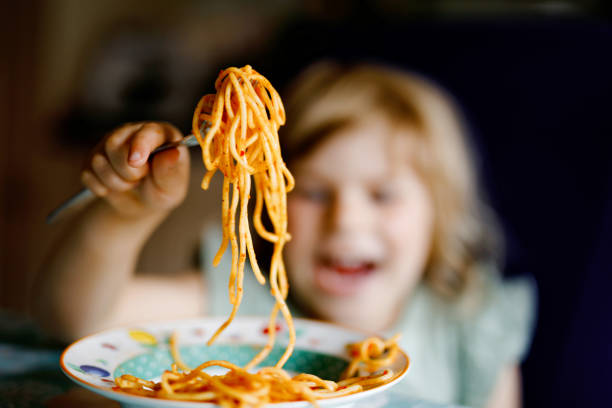 adorable fille tout-petit manger des spaghettis de pâtes avec de la bolognaise de tomate avec de la viande hachée. joyeux enfant d’âge préscolaire mangeant un repas frais et cuisinés avec des nouilles et des légumes à la maison, à l’intérieur. - child eating pasta spaghetti photos et images de collection