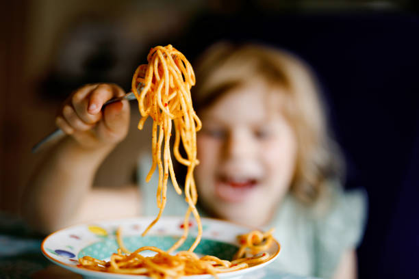 愛らしい幼児の女の子は、ひき肉とトマトボロネーゼとパスタスパゲッティを食べます。屋内、自宅で麺や野菜と新鮮な調理健康的な食事を食べて幸せな就学前の子供。 - child eating pasta spaghetti ストックフォトと画像