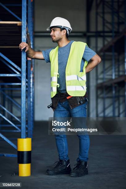 Shot Of A Young Man Experiencing Back Pain While Working At A Construction Site Stock Photo - Download Image Now