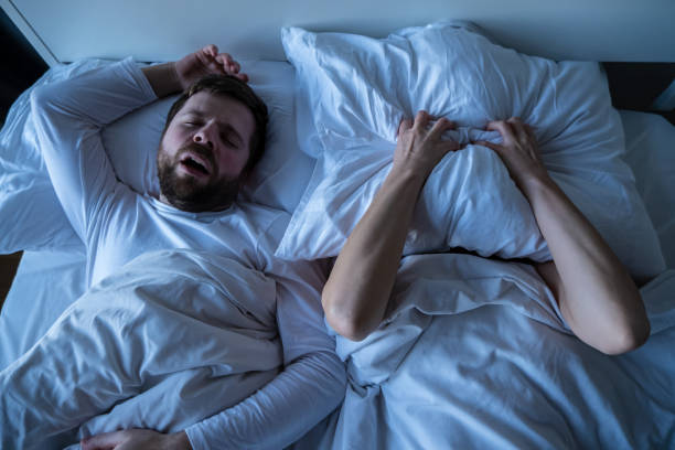 Woman is stressed, covers her face with a pillow, she cannot fall asleep because her husband snores. Concept of female insomnia. Woman is stressed, covers her face with a pillow, she cannot fall asleep because her husband snores in bed at night. Concept of female insomnia. Top view. snoring husband stock pictures, royalty-free photos & images