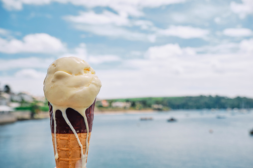 Hand holding an Ice Cream cone by the waters edge at St. Mawes, Cornwall on a sunny June day.