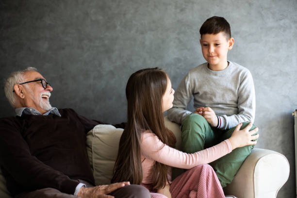 istock Kids are playing on sofa while granddaddy is sitting by them and watching. 1326622292