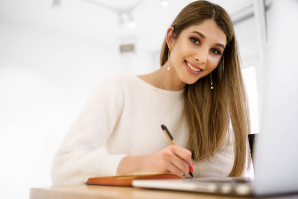 istock Smiling woman in white sweater writing in notebook. 1326623565