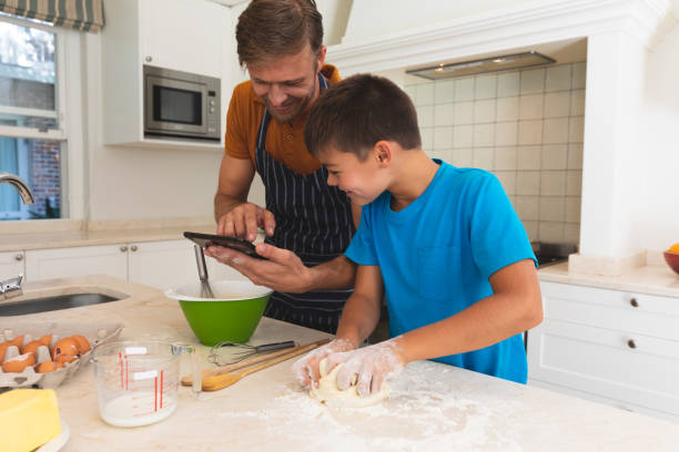 istock Caucasian father using tablet and son baking and smiling in kitchen 1326631117