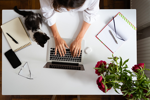 Flat lay home office desk, workspace with woman hands, laptop, red peony bouquet