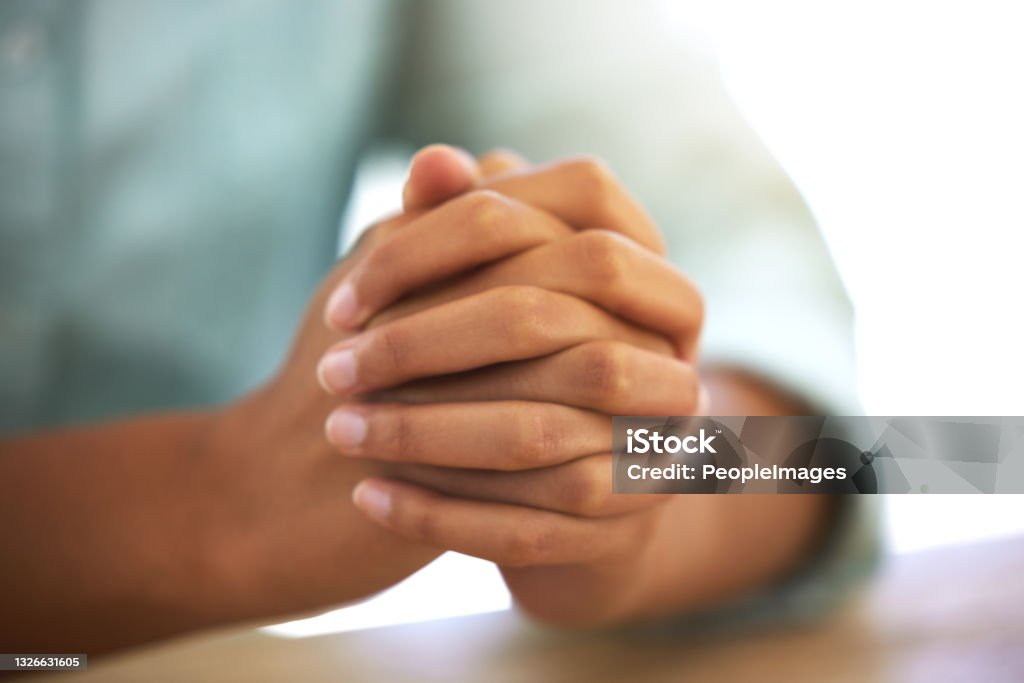 Cropped shot of an unrecognizable person sitting with their hands together I hope this goes well Praying Stock Photo