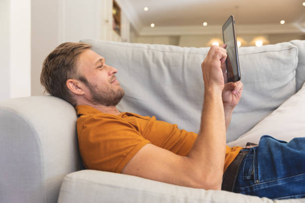 istock Caucasian man lying on couch, smiling and using tablet at home 1326632526