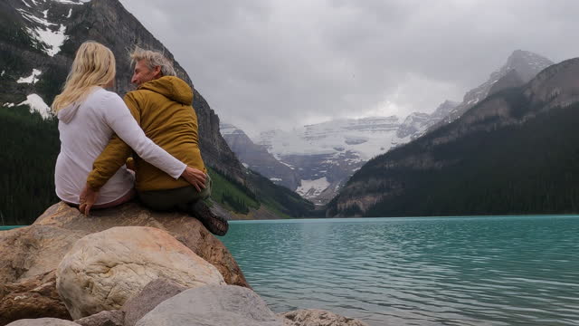 Mature couple enjoy view across Lake Louise during rain storm