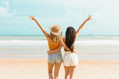 Two Asian women in summer casual clothes play in the sea on vacation in tropical country. Young beautiful Female dance with joy in the beach on a summer day