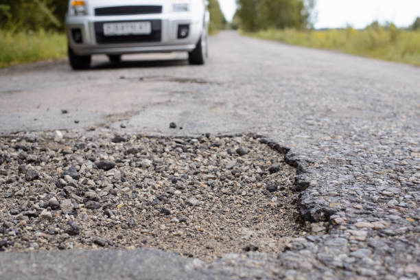 istock Country road in terrible condition. Modern grey vehicle approaching huge pothole 1326641789