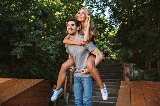 Happy young man carrying his pretty girlfriend on his back at a city park