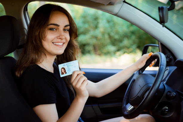 Student in a modern car showing driving licence Smiling girl driver drivers license photos stock pictures, royalty-free photos & images