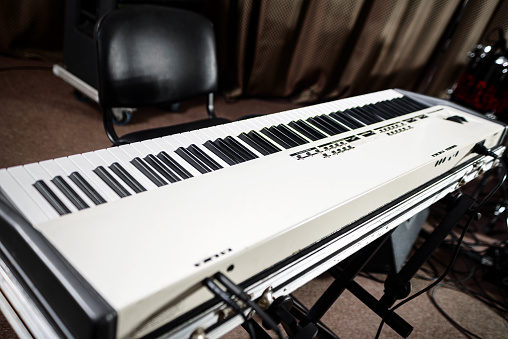 The keyboard of the synthesizer stands on the stage among the musical equipment.