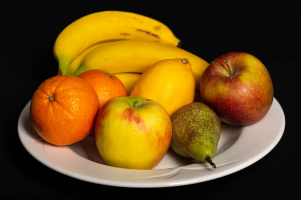 istock White stone fruit bowl against a black background with bananas, oranges, apples a lemon and pear 1326645805