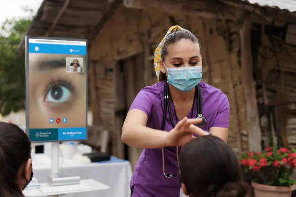 Photo of Latin nurse with wireless device checking patient's eye