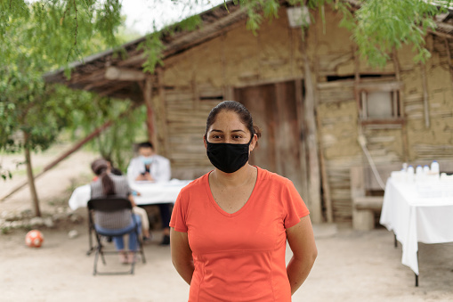 A latin female patient wearing a face mask in a rural area, standing and looking at the camera.