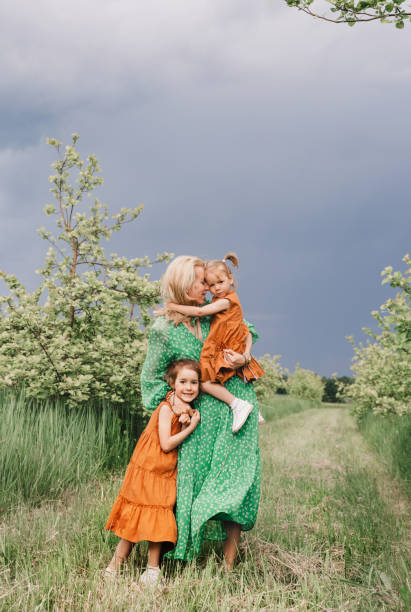 a happy mother in a green dress walks with her two little daughters in the garden before the rain. a happy mother in a green dress walks with her two little daughters in the garden before the rain. family happiness and maternal care mom and sister stock pictures, royalty-free photos & images