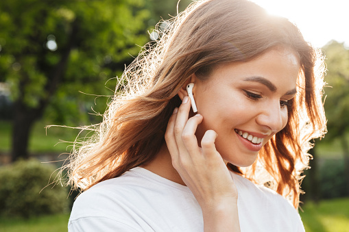 Close up of a smiling pretty young girl in wireless earphones outside