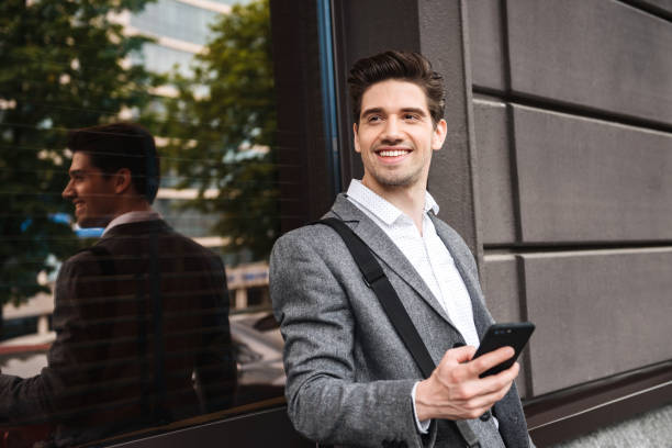 istock Smiling young businessman leaning on a wall 1326650620