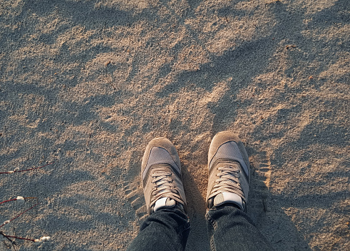 Sports women's gray sneakers on light sand with blue shadows from the setting sun. The concept of evening or morning jogging, fitness and workout. Top view, copy space.