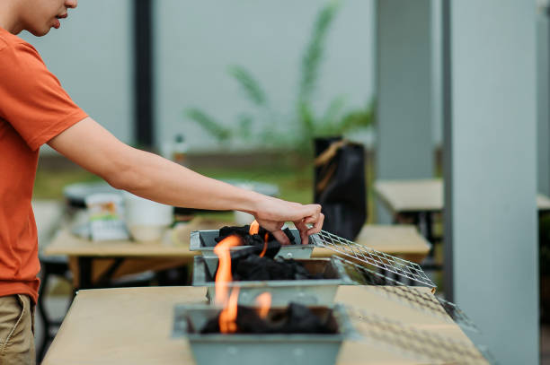 il maschio cinese asiatico alleggerise il fuoco sulla griglia barbecue nel cortile di casa - asian culture barbecue chicken smoke foto e immagini stock