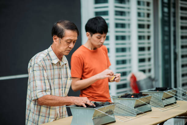 Asian chinese father and son lighten up fire on barbecue grill in front yard of house