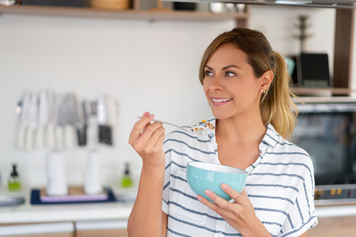 Portrait of a happy Latin American woman at home having cereals in a bowl for breakfast and smiling - lifestyle concepts