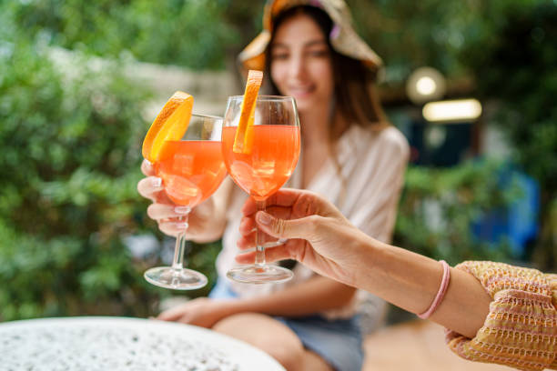 les femmes en terrasse clignent des yeux avec des cocktails de fruits orange. gros plan sur les mains tenant des lunettes. des gens flous. - juice drinking women drink photos et images de collection