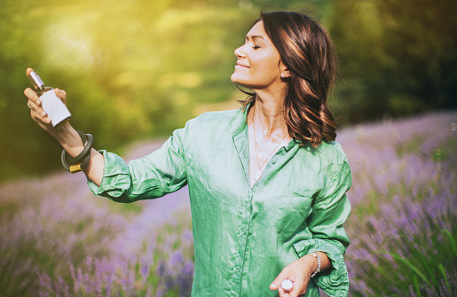 Mid adult woman is spraying with lavender water to refresh herself in the lavender field.