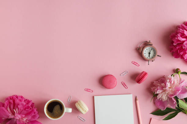 istock Business and education concept. Feminine workplace with notepad, pencil, alarm clock, peony flowers, a cup of coffee and macarons on a pink background with copy space. Top view, flat lay 1326663235