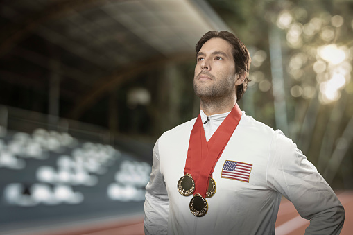 American male athlete smiling after winning a gold medal in a stadium. Sportsman with medal celebrating his victory.