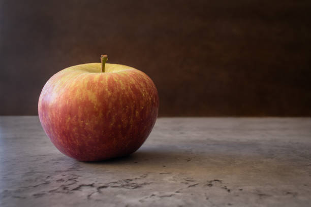 Still life of one fuji apple with left alignment resting on a counter isolated on a dark textured background. Fruit photography with empty space for text