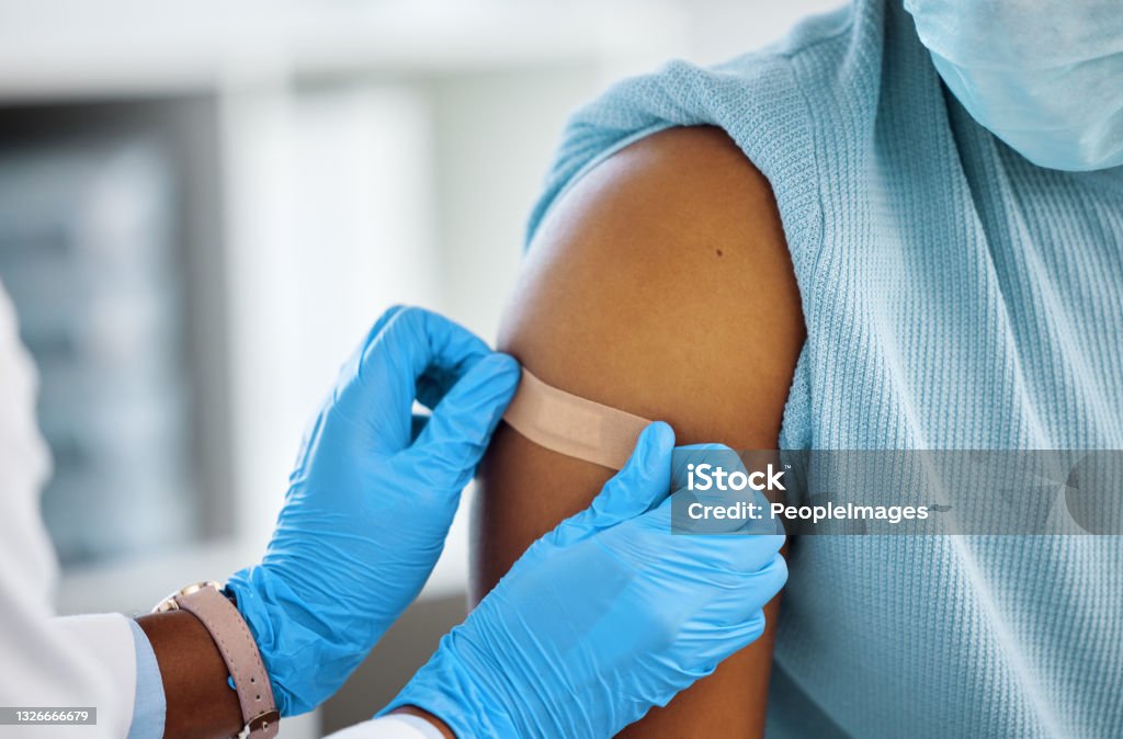 Shot of a doctor applying a plaster to her patients arm Just leave this on for an hour Vaccination Stock Photo