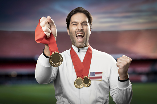 American male athlete smiling after winning a gold medal in a stadium. Sportsman with medal celebrating his victory.