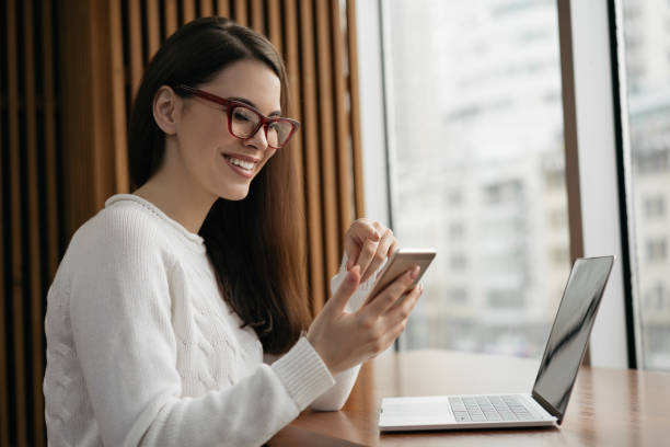 Freelancer using mobile phone, laptop computer, working from home. Successful business woman holding smartphone, planning start up project, sitting in modern office