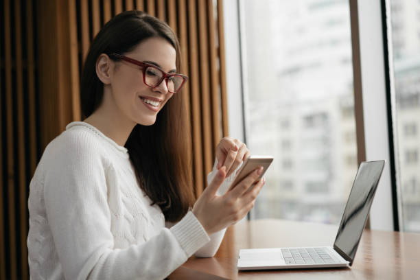 Freelancer using mobile phone, laptop computer, working from home. Successful business woman holding smartphone, planning start up project, sitting in modern office stock photo