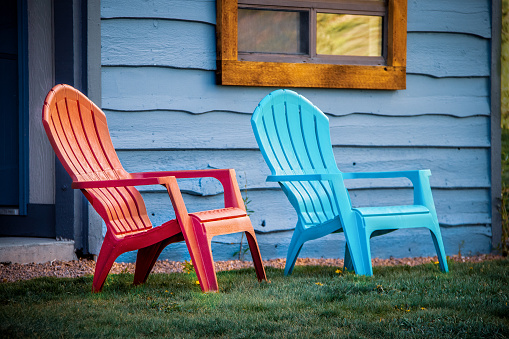 Close-up of red and turquoise arondiack chairs sitting outside blue wooden cabin door on grass.