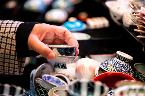 Store display closeup of ceramic pottery with tea cups teacups design and hand person picking buying in Kyoto, Japan Nishiki market street
