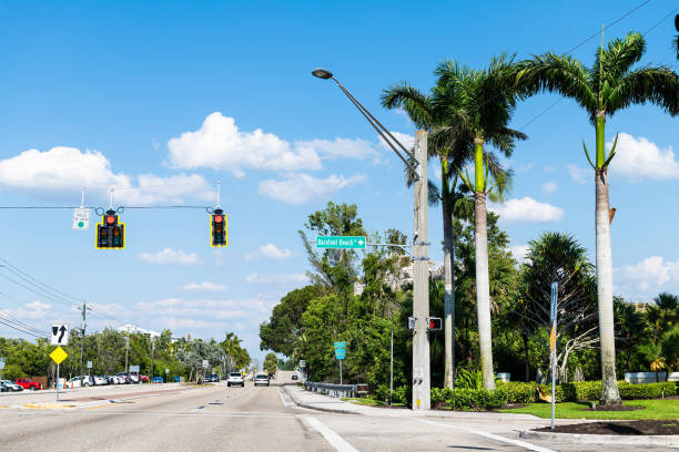 palmiers sur la route de rue à bonita springs, en floride avec signe pour la célèbre ville de barefoot beach le jour dans le comté de collier avec un ciel bleu au printemps - bonita springs photos et images de collection