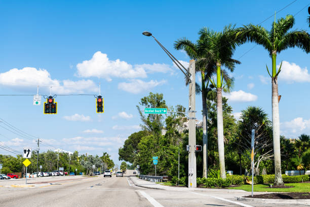 春に青空でコリアー郡の日に有名な裸足ビーチ市の町の看板を持つボニータスプリングス、フロリダ州の道路上のヤシの木 - bonita springs ストックフォトと画像