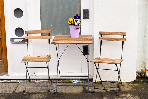 Empty wooden table outside restaurant cafe shop with two chairs on sidewalk street and purple yellow pansy flowers in flowerpot nobody