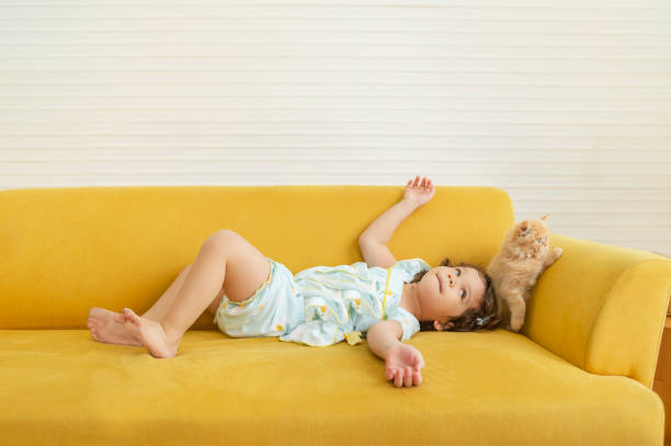 Kids laying on the yellow sofa bed with their kitten stock photo