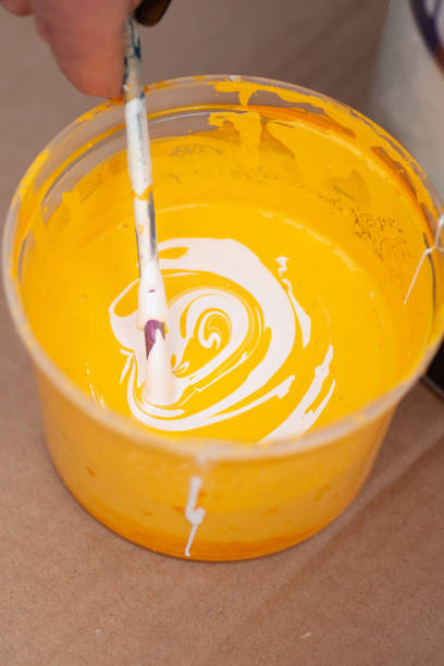 istock macro hand mixes yellow and white paint with a wooden stick in a plastic container 1326689511