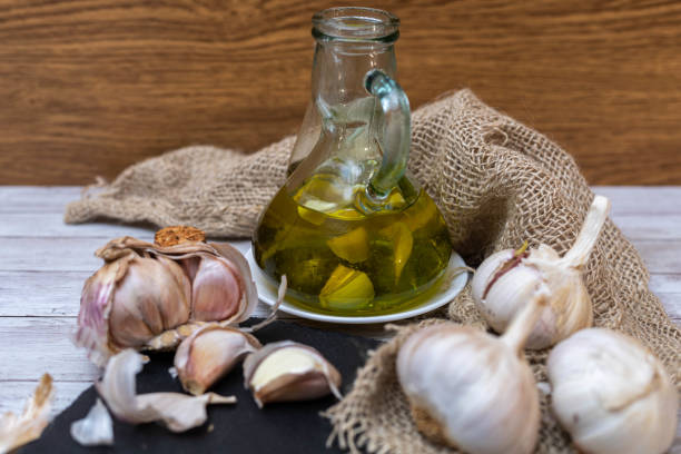 selective focus of an extra virgin olive oil surrounded by garlic to create aromatic oil for meals on a wooden table and sackcloth or burlap.
