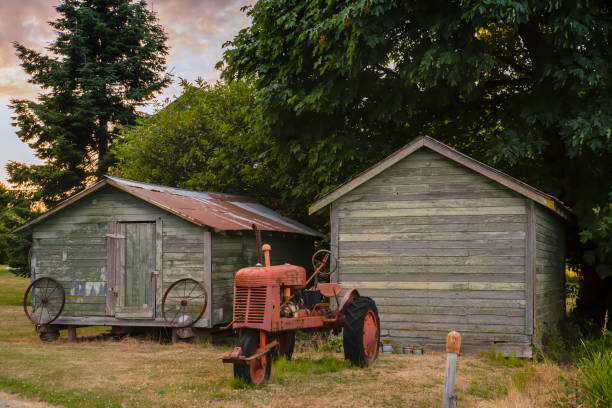 Old red tractor stands near a wooden barn