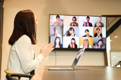 High-Tech Meetings Concepts:  Young female Entrepreneur in an office boardroom are joined by participants joining by video call.  Employees are applauding and celebrating their success by Online