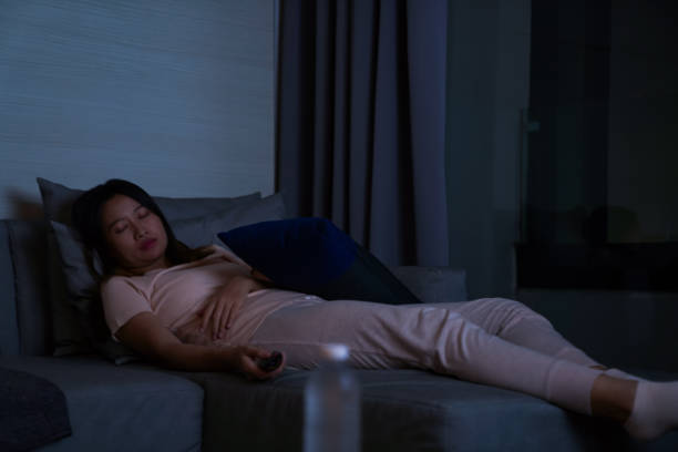 Asian woman sleeping on sofa while watching television at night Beautiful Asian woman in pajamas sleeping on sofa in living room while watching movie on TV in apartment at night. Female relax and enjoy city night life and indoor lifestyle on couch at home. sofa bed stock pictures, royalty-free photos & images