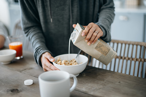 Foto recortada de una joven madre asiática preparando un desayuno saludable, vertiendo leche sobre cereales en el mostrador de la cocina. Estilo de vida de alimentación saludable photo