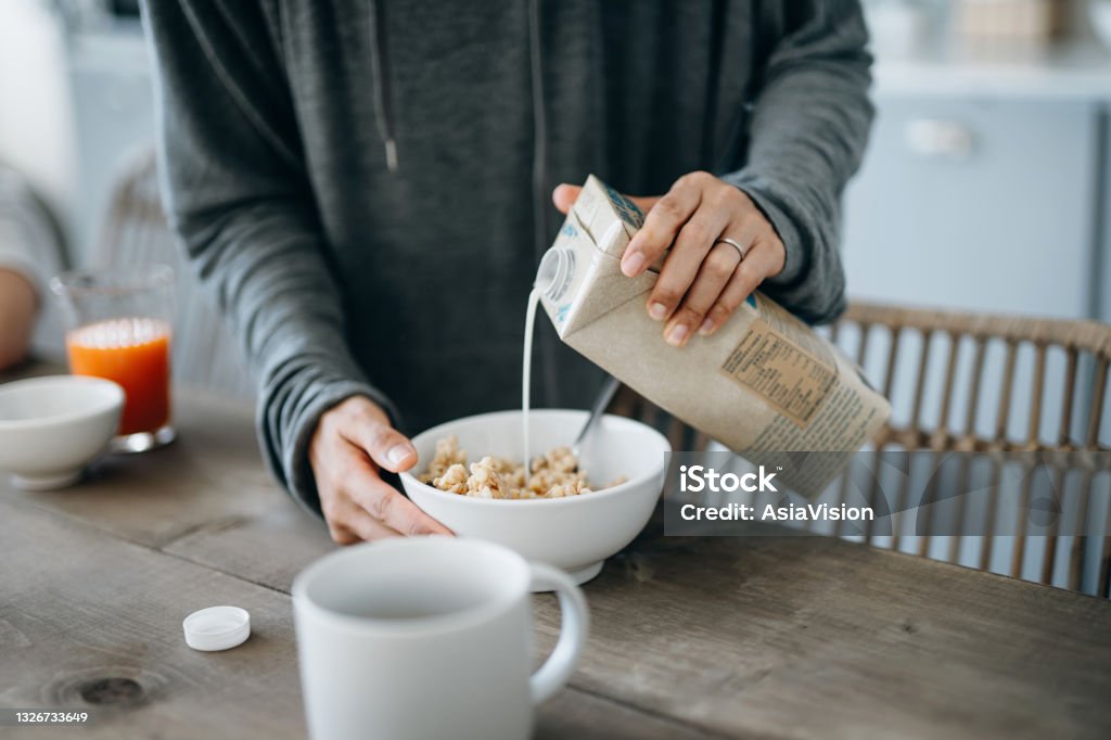 Cropped shot of young Asian mother preparing healthy breakfast, pouring milk over cereals on the kitchen counter. Healthy eating lifestyle Milk Stock Photo