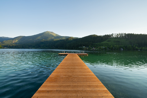 inviting for refreshment in lake, wooden jetty in calm water of lake with low mountains in baclground on sunny summer vacation day